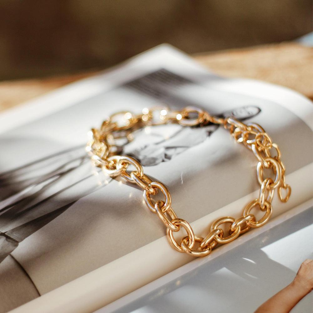 A 14k gold bracelet lays on top of a fashion magazine