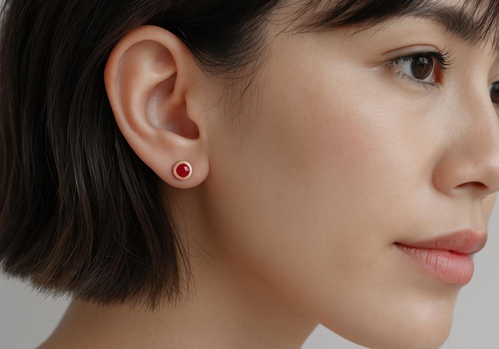 A woman laying on a backdrop of plants staring up into the camera, on her left hear she is wearing a ruby earring