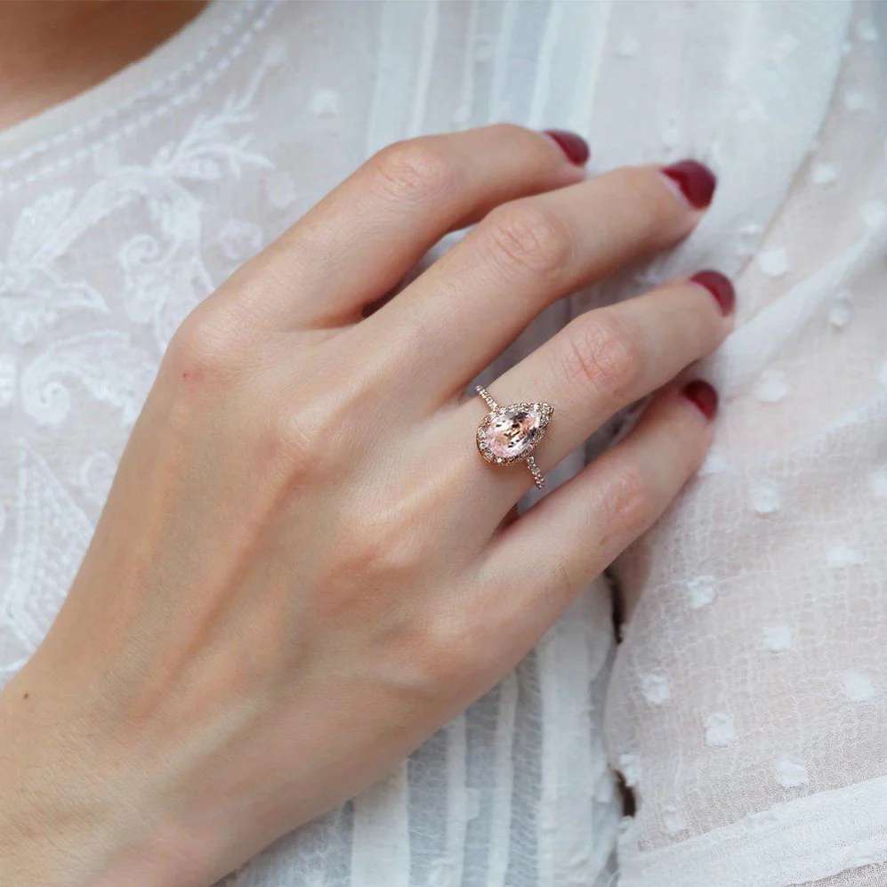 A hand with red painted nails wears a Morganite ring on their ring finger